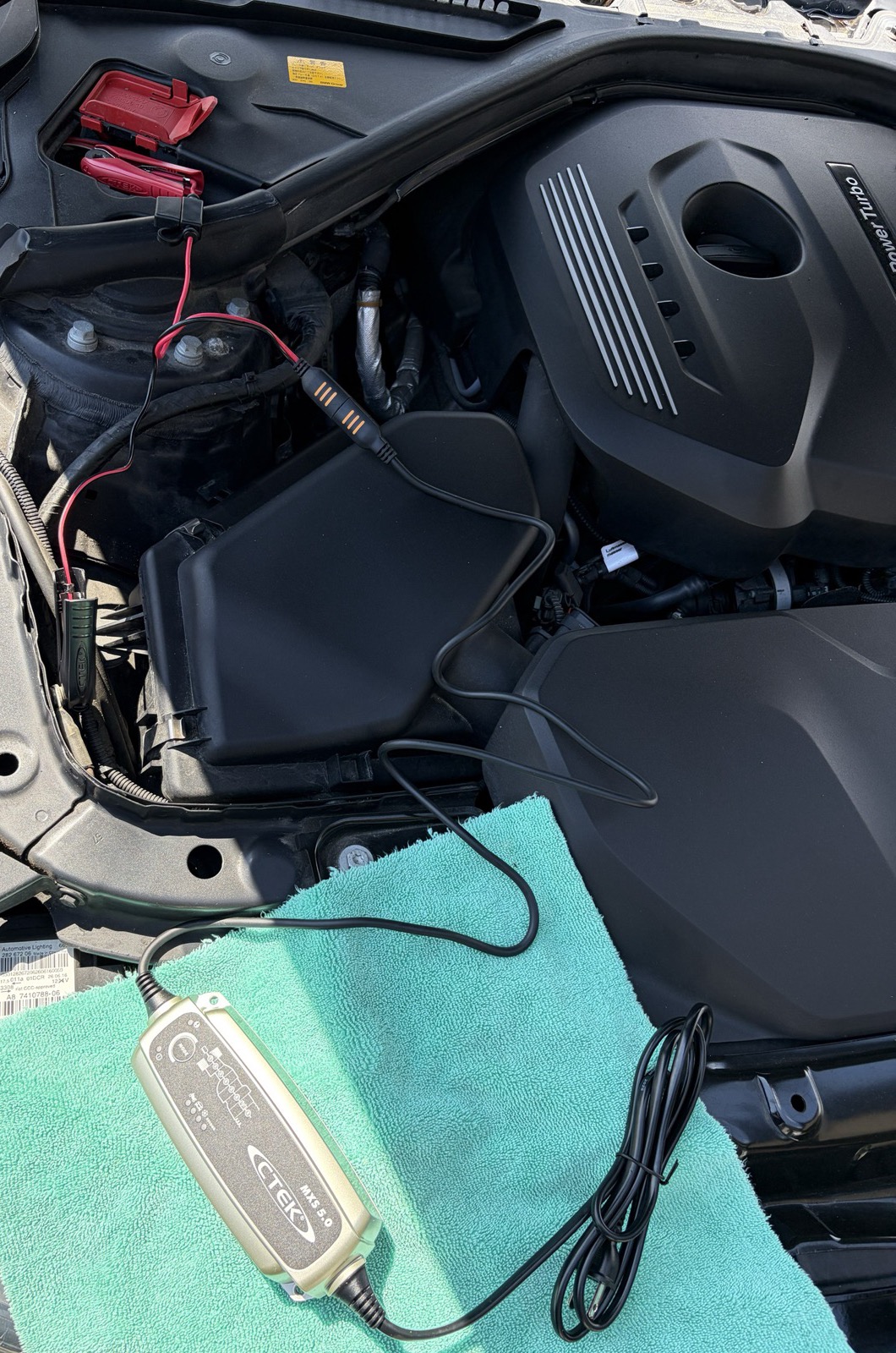 BMW 420iのエンジンルームで、赤いカバーのプラス端子と車体のマイナス端子に充電器のクリップをつないだところ